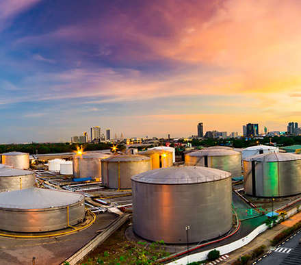 Multiple above ground storage tanks group together in a port with a city skyline in the background